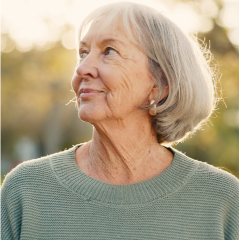 Older woman with gray hair in a green knit sweater outdoors, gazing to the left with a gentle smile.