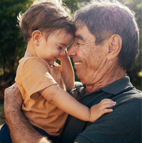 Grandfather lifting and cuddling his smiling toddler in a warm moment of bonding outdoors.